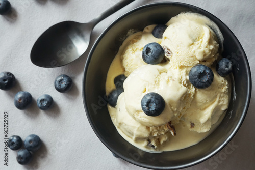 Ice cream with fresh blueberries in a dark plate next to a spoon