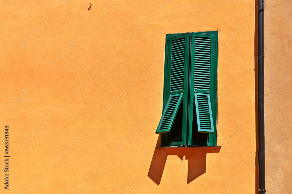 window with half-closed shutters on an orange concrete wall window with half-closed shutters on an orange concrete wall