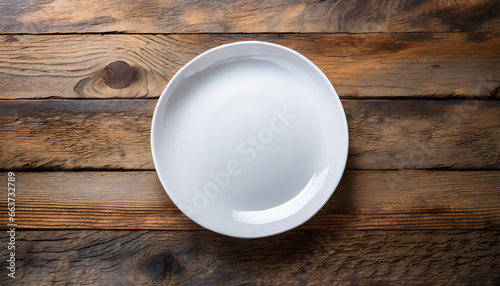 White plate resting on a wooden surface with space for text. Top view. Copy space