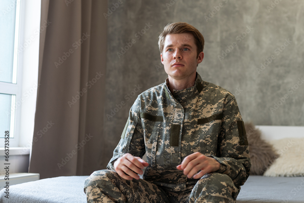 Stressed veteran soldier engrossed in depressive thoughts and memories. Sad depressed young military man in camouflage uniform sitting on couch and thinking about war. PTSD and therapy concept.