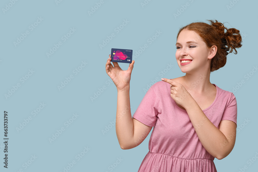 Beautiful young woman pointing at credit card on blue background Beautiful young woman pointing at credit card on blue background