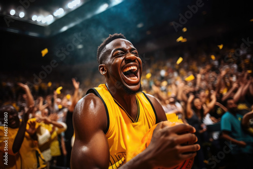 african black basketball player in a yellow uniform rejoices at the abandoned ball in a stadium with spectators