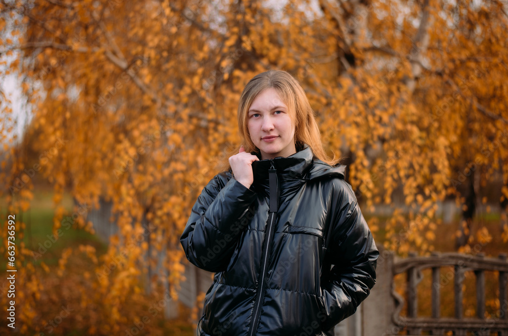 Portrait of a beautiful girl in a dark jacket standing near colorful autumn leaves. A young woman relaxes in a park against the background of yellow trees in the autumn season. Portrait of a beautiful girl in a dark jacket standing near colorful autumn leaves. A young woman relaxes in a park against the background of yellow trees in the autumn season.