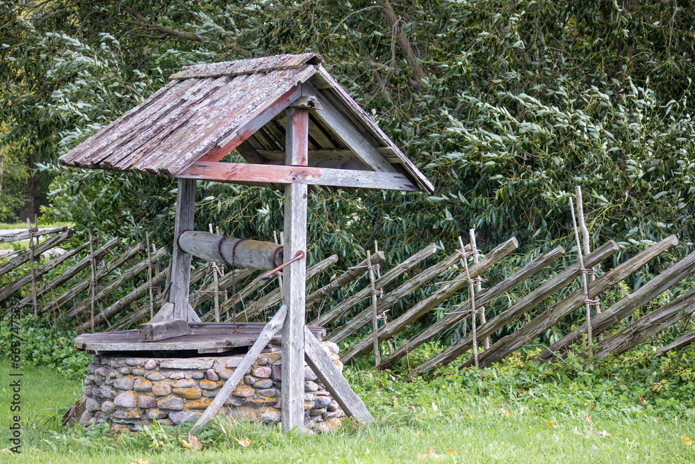 a wooden water well with a roof and a wicker wooden fence behind it a wooden water well with a roof and a wicker wooden fence behind it