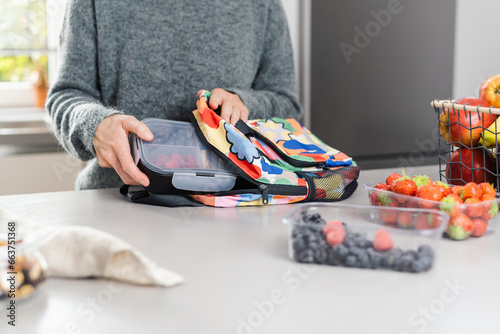 Mom packs a lunch box with snacks lunch in a school backpack in the kitchen.