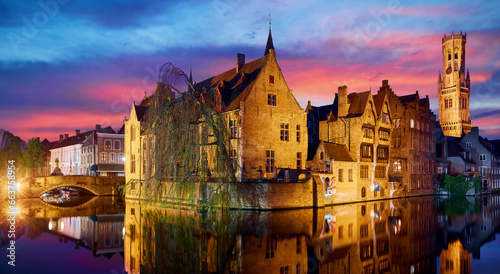 Bruges, Belgium. Evening sunset with blue sky. Water channels of ancient medieval town view to Belfort van Brugge tower, famous landmark.