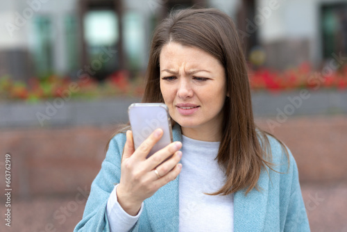 Young woman squints and sees poorly without spectacles. girl trying look closer at the smartphone phone screen. Concept poor eyesight female, wear glasses, ophthalmology