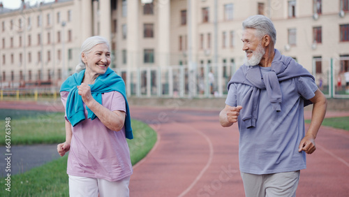 Couple old men running marathon stadium arena. Grandparent jog together. Romantic elderly smiling people sport training. Granny and Grandpa workout. Love athletes. Active senior lifestyle. Health care photo