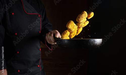 Professional chef prepares crispy nagits in a steamed hot pan. Flying nagits over the frying pan in the cook hand. Place for prescription on dark background photo