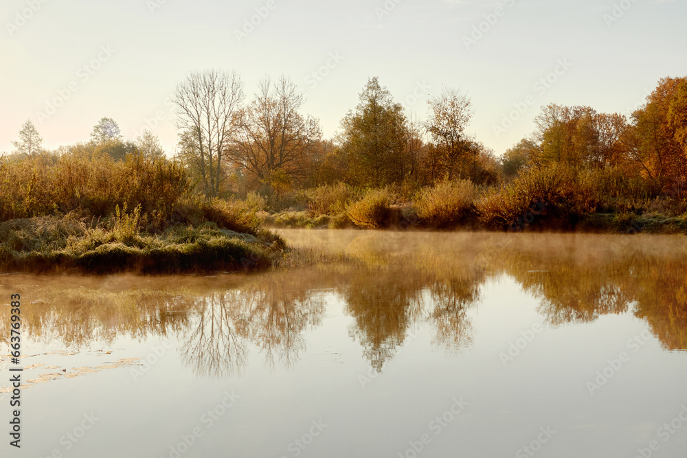 Small river in an autumn woodland. Morning fog over the river.