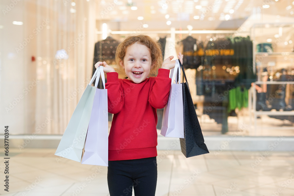 Happy child girl in red sweater with shopping bags in cloth store. Black Friday concept Happy child girl in red sweater with shopping bags in cloth store. Black Friday concept