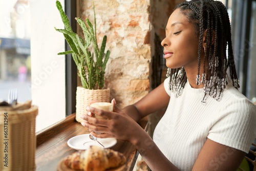 Young pensive black woman student enjoying coffee taste in canteen photo