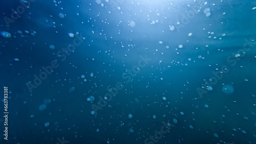 Underwater shot of sun rays shining through clear sea water with rising up air bubbles