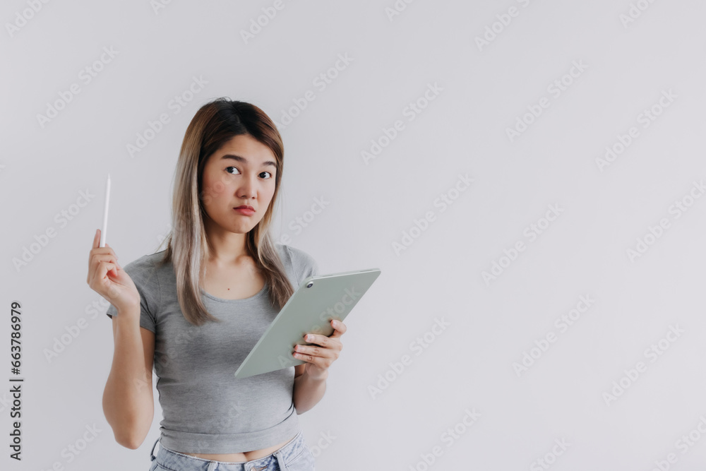 Asian Thai woman wear grey, hands holding tablet and white pen, no idea suspicious, doubt face while working and looking at the camera, isolated on white background. Asian Thai woman wear grey, hands holding tablet and white pen, no idea suspicious, doubt face while working and looking at the camera, isolated on white background.