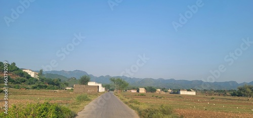 Winding road running through a barren landscape, with a few homes and hills in the distance © Wirestock