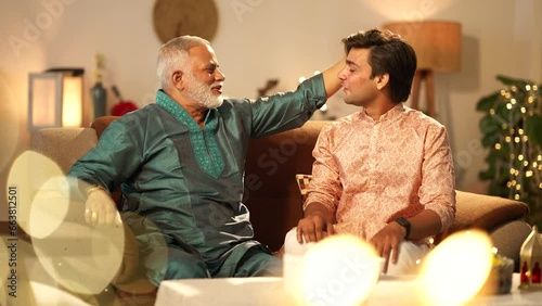 Indian son touching her father's feet on diwali on the sofa and talk to her.they both good looking in traditional dress.decorated background.diwali festival celebration.