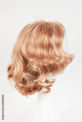 Natural looking blonde fair wig on white mannequin head. Short hair cut on the plastic wig holder isolated on white background, side view.