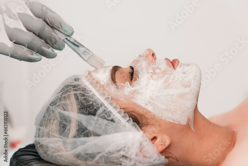 Crop unrecognizable beautician applying white mask with brush to face of lady lying on back in spa photo