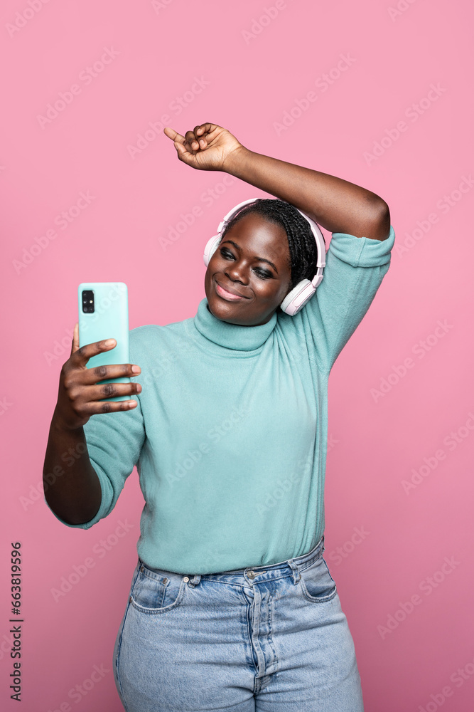African lady captures selfie with smartphone on pink backdrop African lady captures selfie with smartphone on pink backdrop
