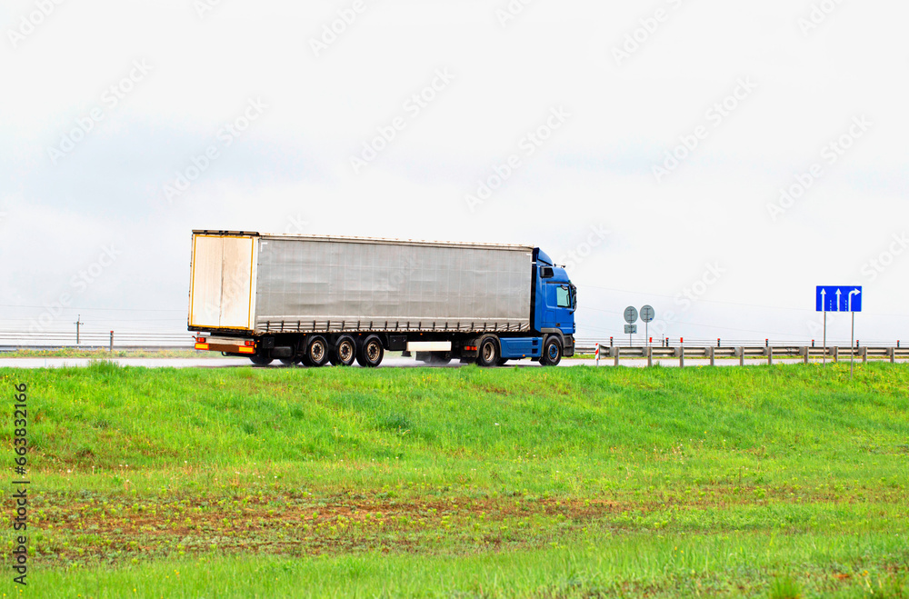 A truck with a semi-trailer transports cargo in summer in cloudy rainy weather on a wet road in the rain. Skidding on the road. Import substitution, export and import of goods. 