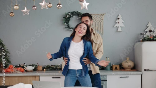 Elated couple dances with joy in a festively adorned kitchen, embodying the heart and warmth of Christmas celebrations and winter merriments New year Eve happy wife and husband spend time together. photo