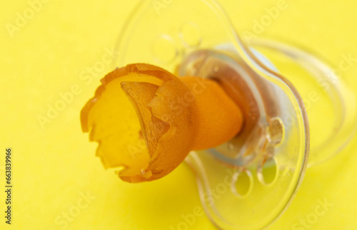 A chewed baby pacifier on a yellow background. Concept of teething in children, close-up.