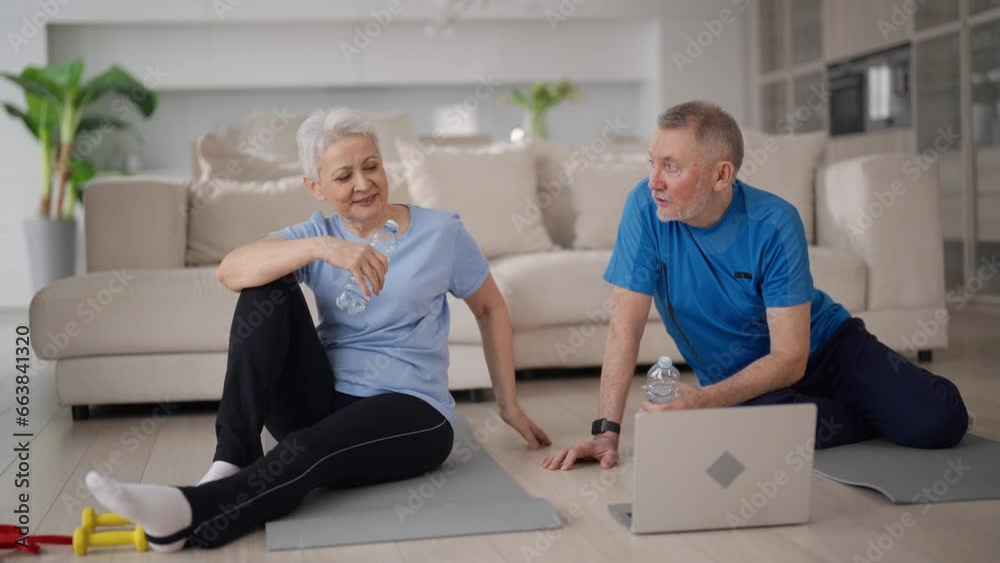 Senior couple man woman resting sitting on mats after online yoga practice on laptop at home. Family wife husband talking discussing training drinking water, Sport, active healthy lifestyle concept. Senior couple man woman resting sitting on mats after online yoga practice on laptop at home. Family wife husband talking discussing training drinking water, Sport, active healthy lifestyle concept.