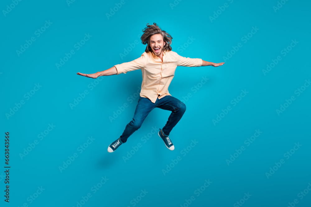 Full length photo of carefree guy with long haircut wear stylish shirt flying hold hands like wings isolated on blue color background