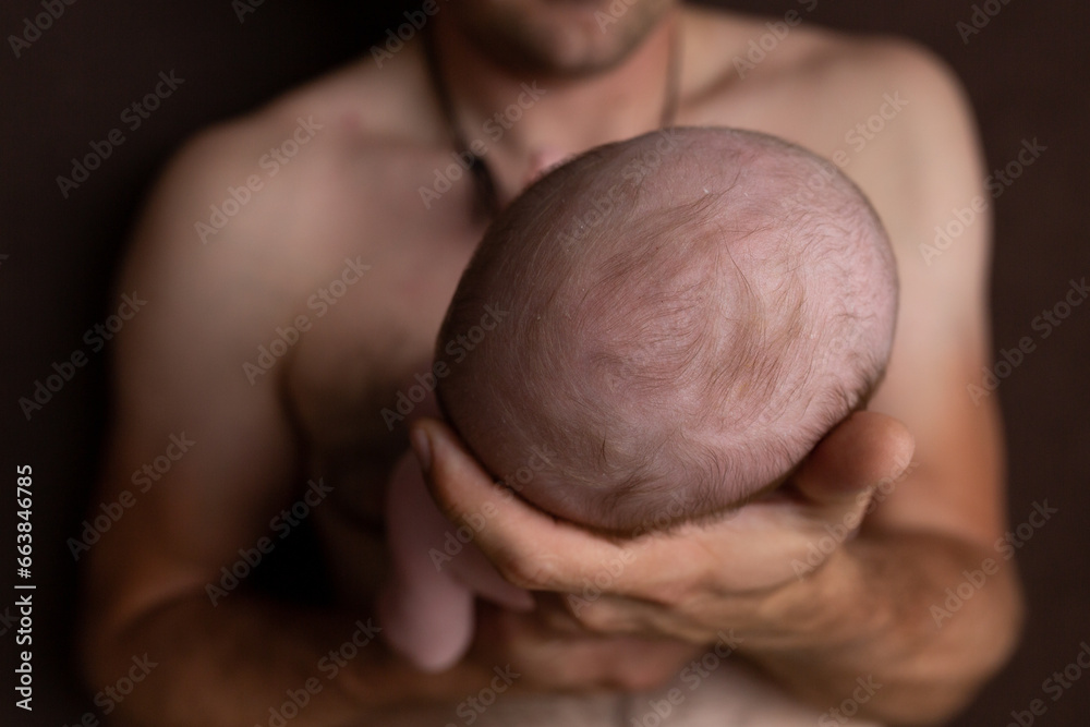Naklejka premium Father holding head of her newborn baby in hands. Loving father hand holding cute sleeping newborn baby child. Beautiful conceptual image of parenthood