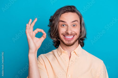 Portrait of satisfied funny guy with long haircut wear stylish shirt showing okey approve excelent work isolated on blue color background photo