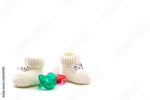 White knitted baby booties with bows and turquoise pink pacifiers on an isolated white background