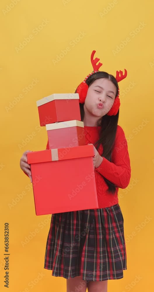 Vertical clip. Cute little girl wearing a Christmas costume holding gift boxes on a yellow background. Vertical clip. Cute little girl wearing a Christmas costume holding gift boxes on a yellow background.