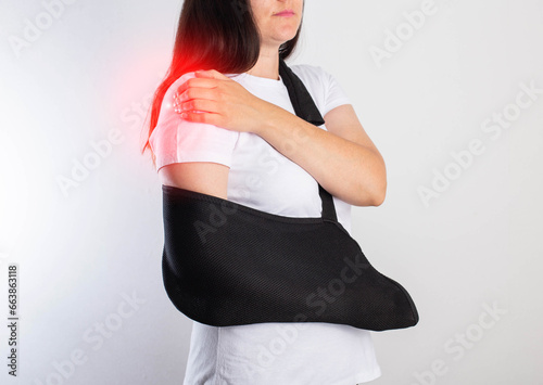 Quadro em tela A girl on a white background with a black supporting medical bandage after a dislocation of the shoulder joint and a bone fracture