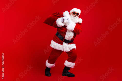 Photo of nice cool senior man wear santa claus clothes hands hold sack bag new year night miracle isolated on red color background © deagreez