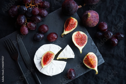 Ripe figs  red grapes with Camembert cheese next to cutlery on a dark background