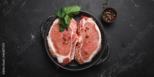 Cut raw meat pork steaks with seasonings in black cast iron pan, dark rustic stone background top view, ready for roasting. Pork loin chops cooking