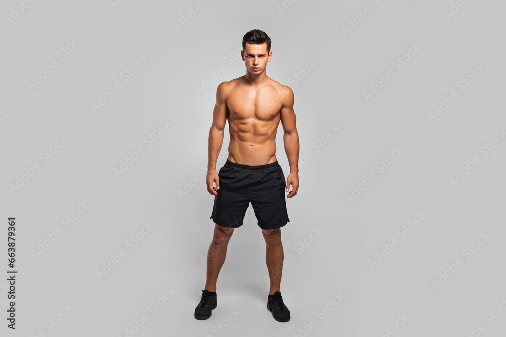 Full length image of a man with an athletic and fit body, posing in the studio with a bare torso, showing six abs pack, looking at camera, grey background. Full length image of a man with an athletic and fit body, posing in the studio with a bare torso, showing six abs pack, looking at camera, grey background.
