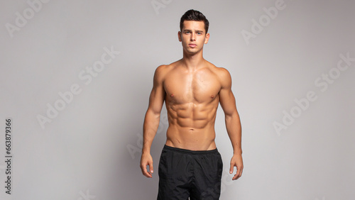 Handsame young man with an athletic and fit body, posing in the studio with a bare torso, showing abs six pack, isolated on the grey background.