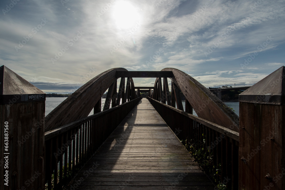 Sunlit Wooden Bridge Over Calm Water Reflecting Blue Sky