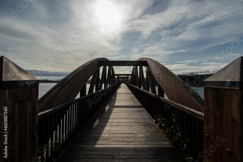 Sunlit Wooden Bridge Over Calm Water Reflecting Blue Sky