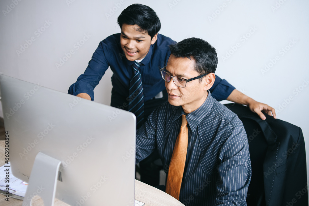 Fototapeta premium Confident young Asian businessman working with mature coworker sitting in front of computer at the office.