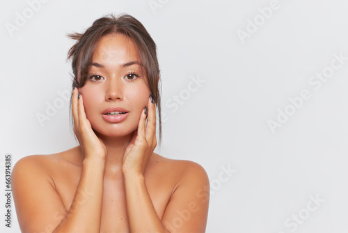 Portrait of beautiful asian woman with naked shoulders posing over white background with hands on her cheeks, relax concept, copy space