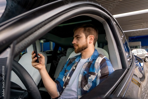 Caucasian bearded guy using mobile phone while typing message during trip on the car. Travel, lifestyle, transport concept