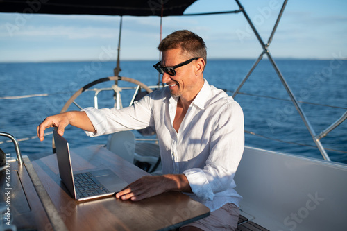 Confident man in sunglasses working on a laptop while sailing on a yacht