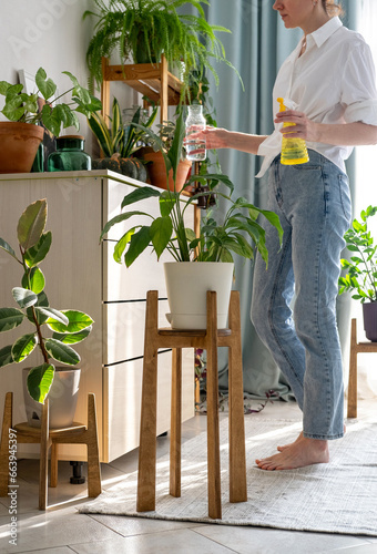 Woman sprays plants in flower pots at home. Indoor gardening. Caring for houseplants home. Interior with lots of plants. #663945397