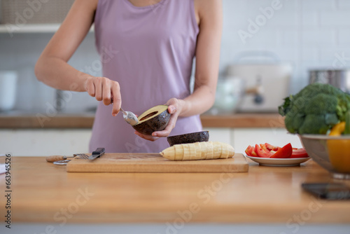 Asian woman in gym clothes cutting an avocado and preparing her healthy breakfast in the kitchen before going to the gym.