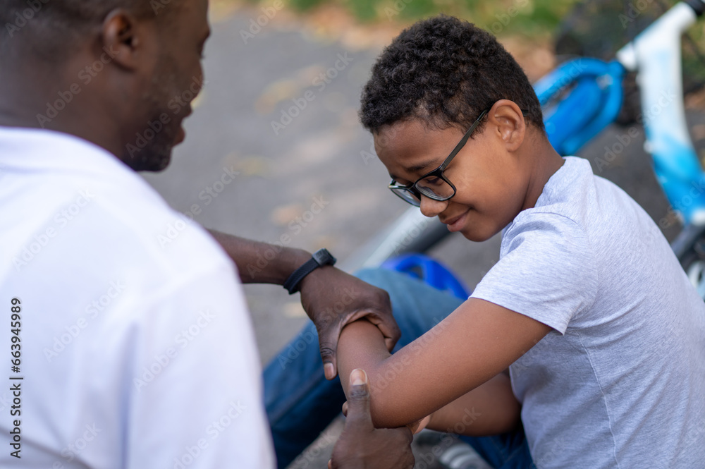 Obraz premium Dad helping his son after falling donw from the bike