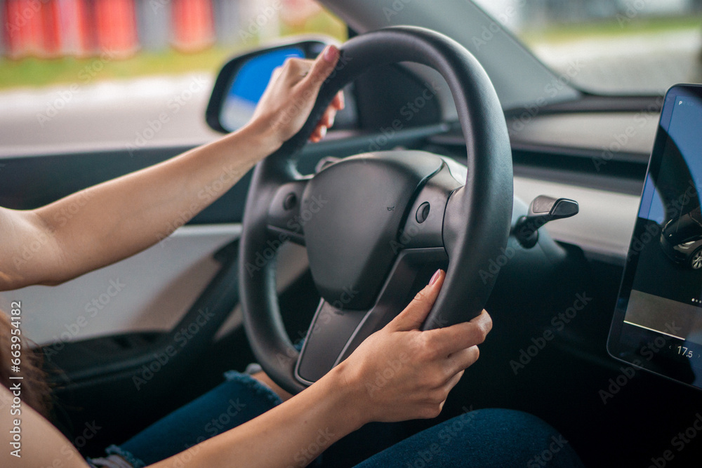 Young lady driving a car while holding hands on the steering wheel. Cropped photo. Auto interior. Travel, lifestyle, transport concept