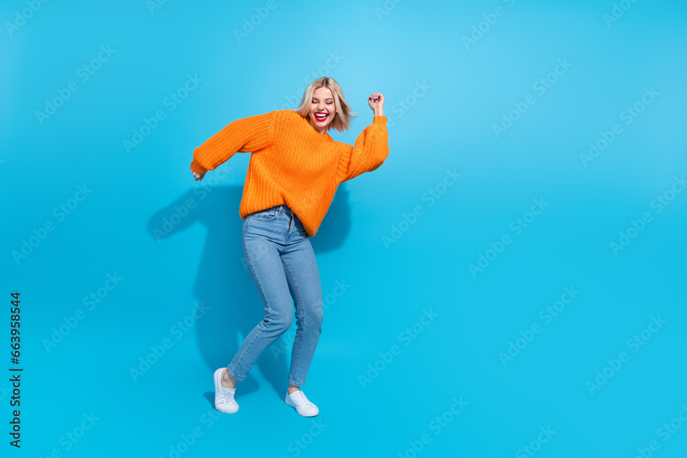 Full size photo of positive cheerful girl with blond hairdo wear knit orange jumper dancing laughing isolated on blue color background