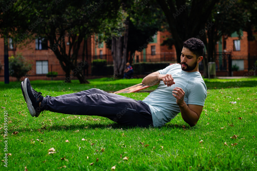 young fitness man doing abdominal exercise in a park in the city